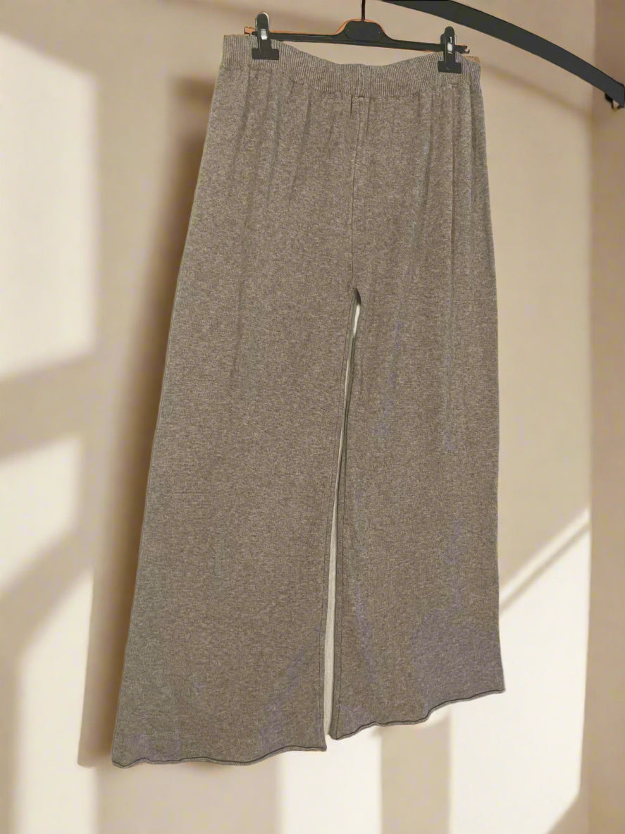 Beige pants hanging on a black hanger against a white wall