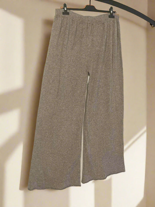 Beige pants hanging on a black hanger against a white wall
