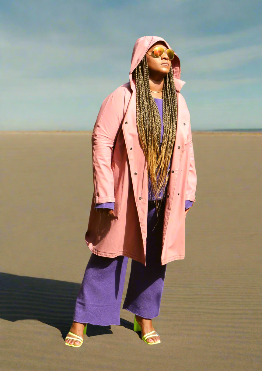 Woman wearing a pink coat and purple pants against a beige background