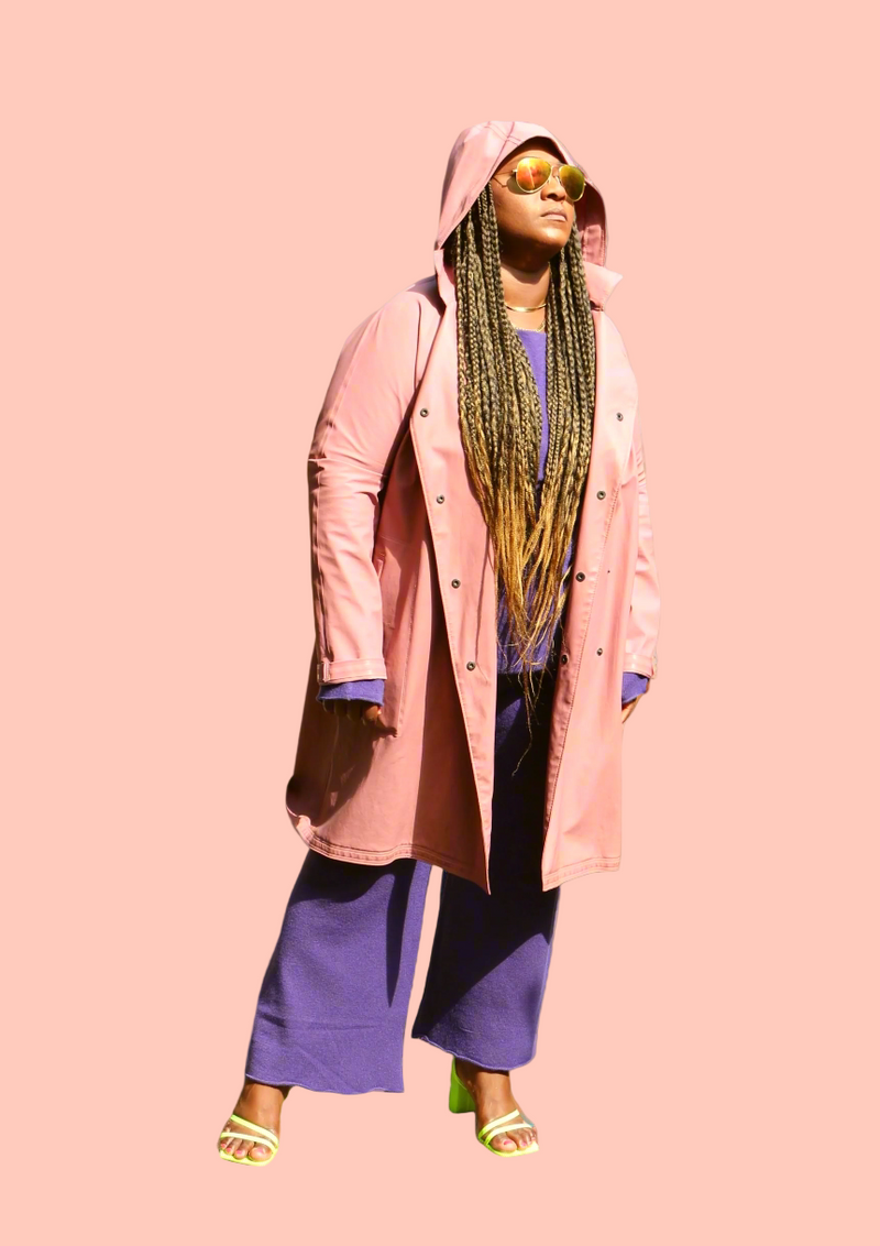 Woman wearing a pink coat and purple pants against a beige background
