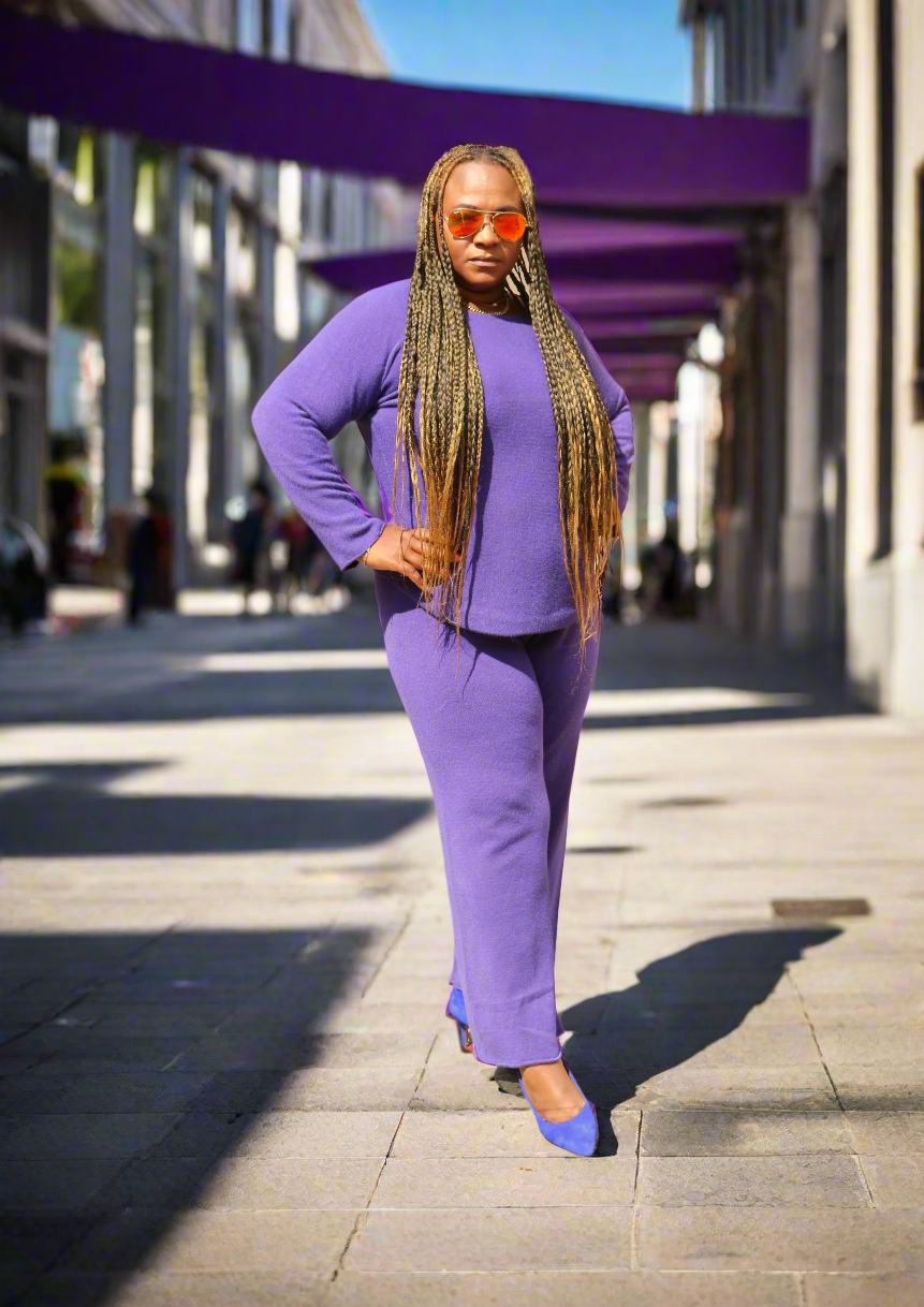 Person wearing a purple outfit with sunglasses on a beige background